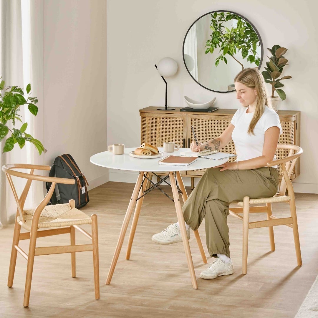A woman sitting at a modern dining table, writing in a notebook, with sleek and minimalist furniture from Structube in a bright, airy room.