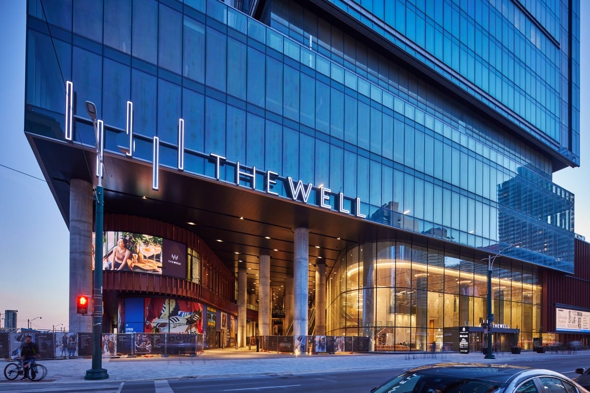 The Well Toronto building exterior at dusk, featuring modern glass architecture with prominent signage, showcasing the entrance to this vibrant urban destination known for its shopping, dining, and entertainment.
