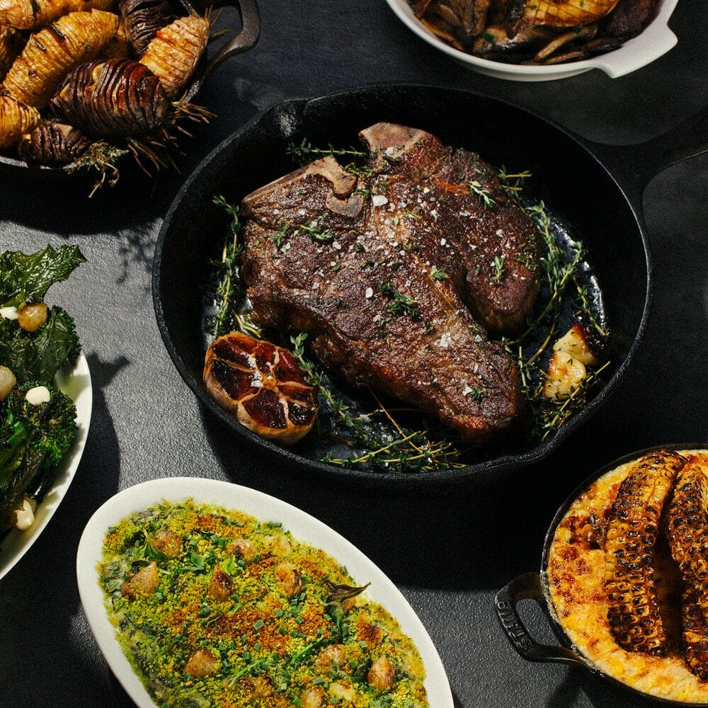 A gourmet feast with a skillet of steak in the middle.