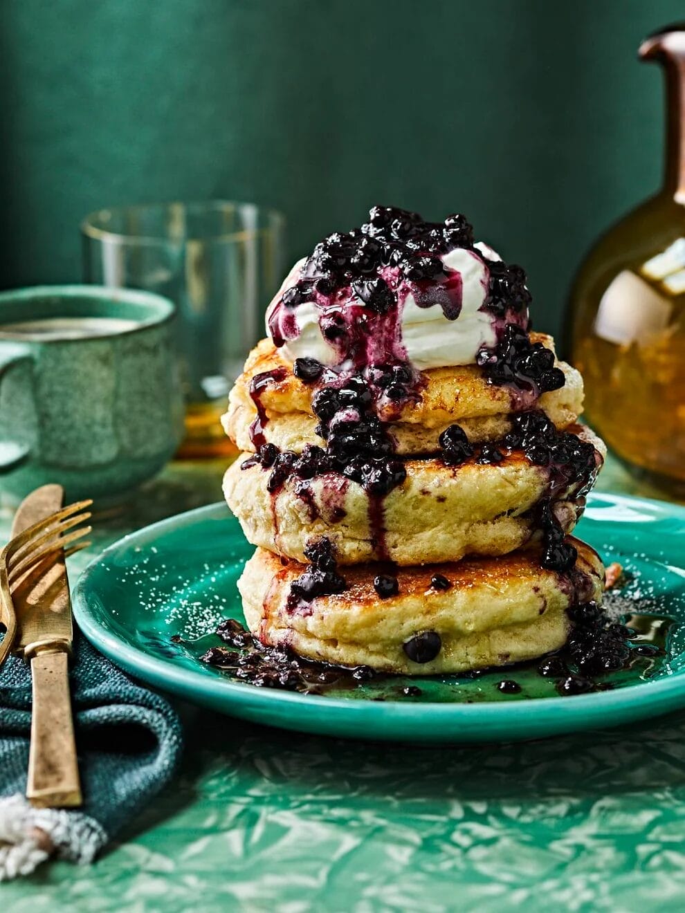 A towering stack of pancake with whipped cream and blueberry syrup.