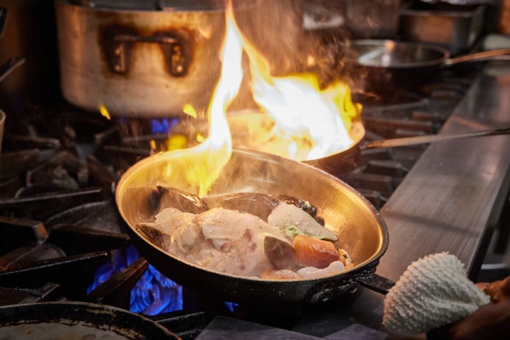Mixed seafood being seared on a high heat stove.