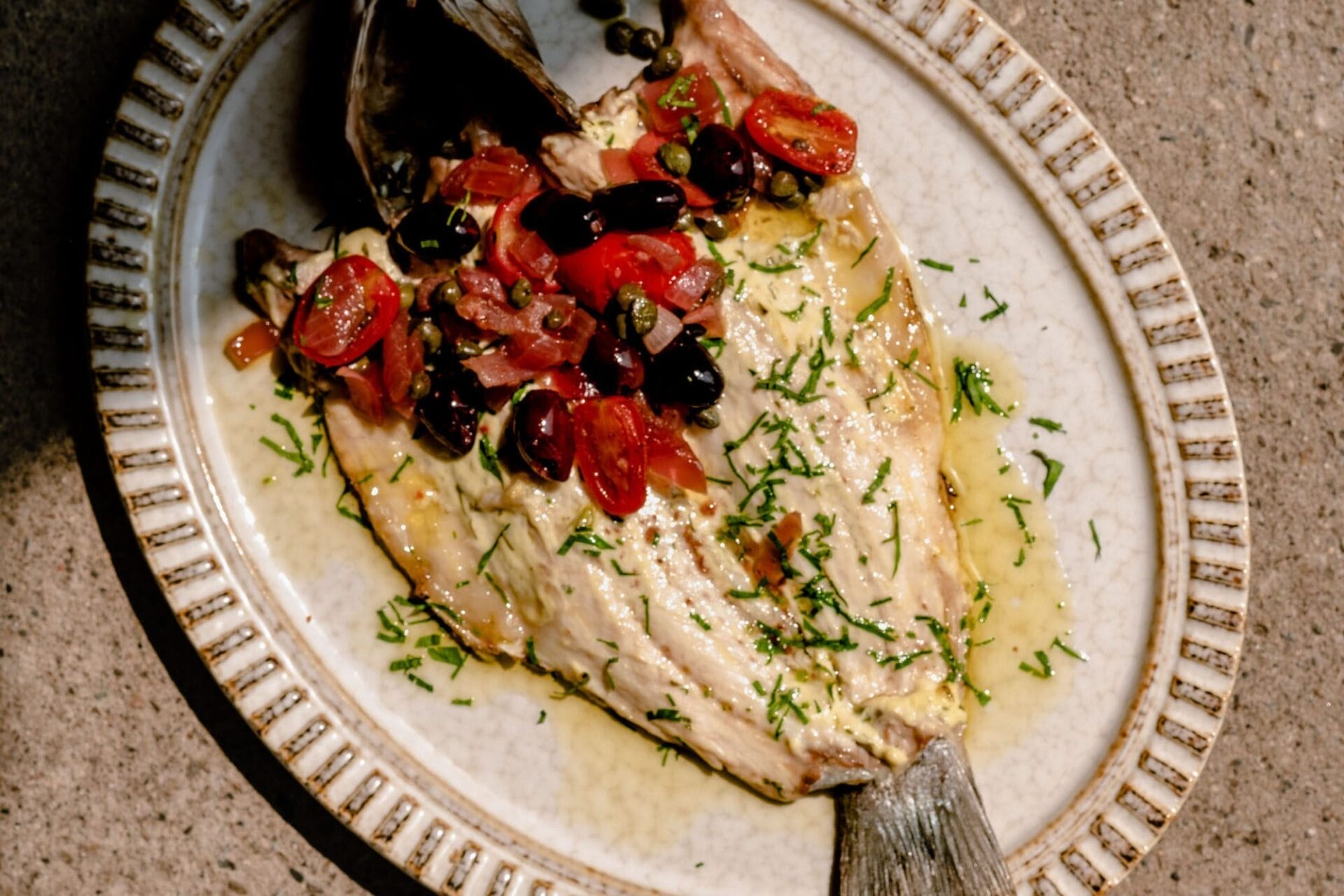 A grilled sea bass topped with olives, and tomatoes.