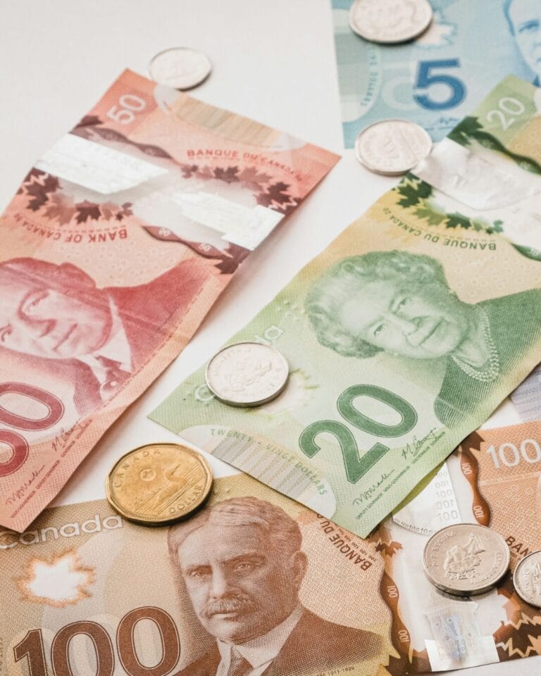 Canadian banknotes in denominations of 5, 20, 50, and 100 dollars, along with various coins, scattered on a surface.