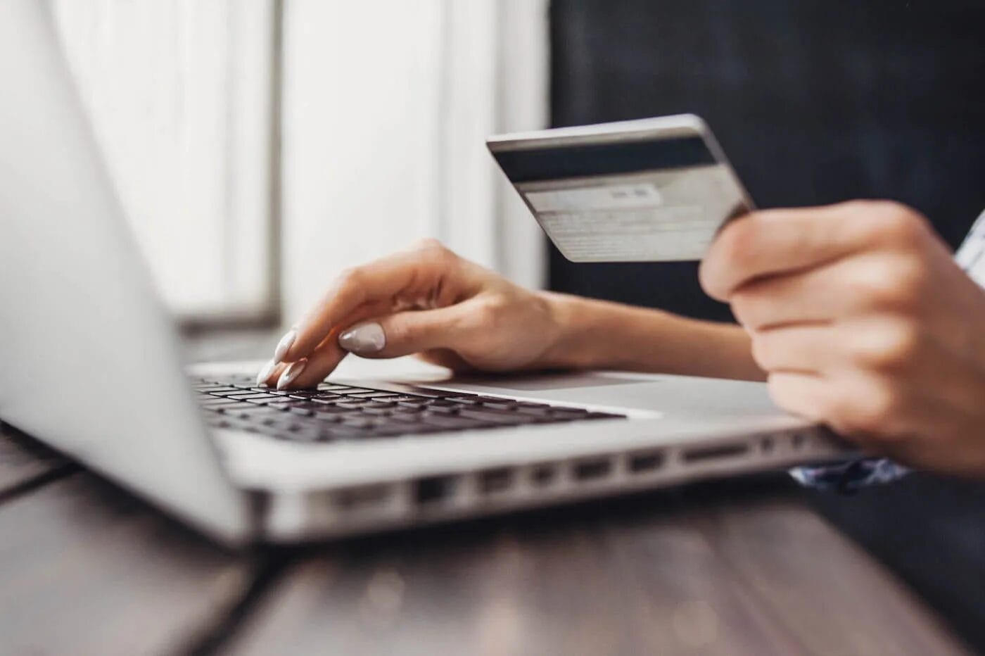 A person using a laptop while holding a credit card, appearing to make an online payment.