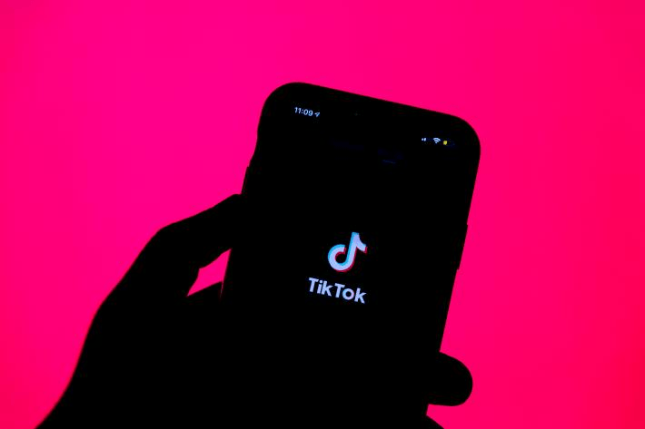 A silhouette of a hand holding a smartphone displaying the TikTok logo on the screen, set against a vibrant pink background, creating a bold and modern visual effect.