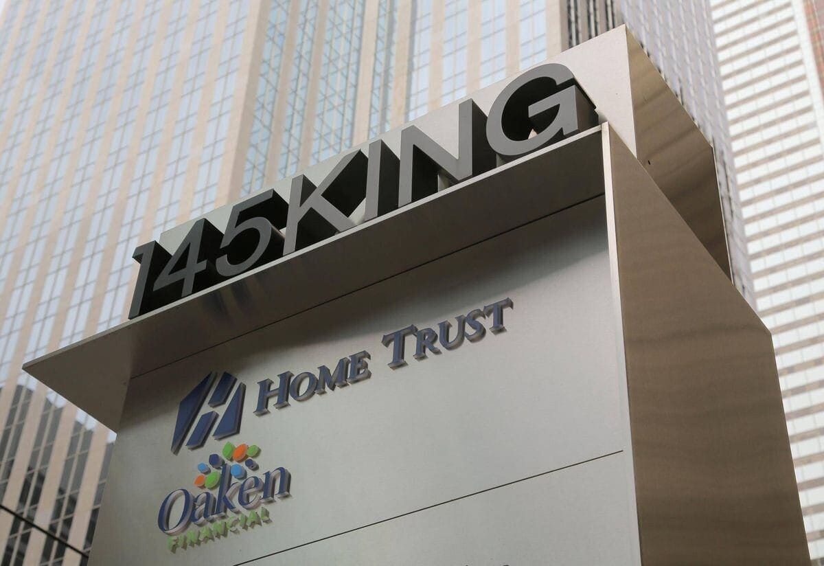 A sign at 145 King Street displaying the logos of Home Trust and Oaken Financial, with a backdrop of tall glass office buildings.