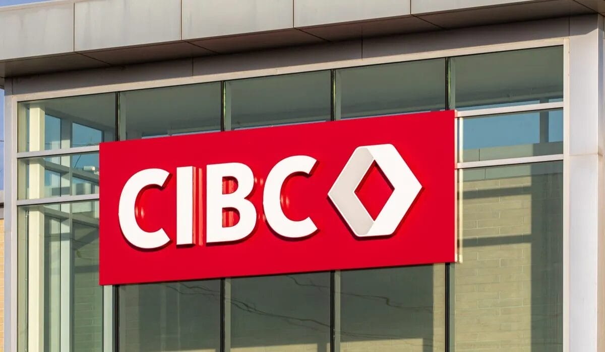 A CIBC bank branch with a red and white sign displaying the bank's name and logo, mounted on a modern glass building.
