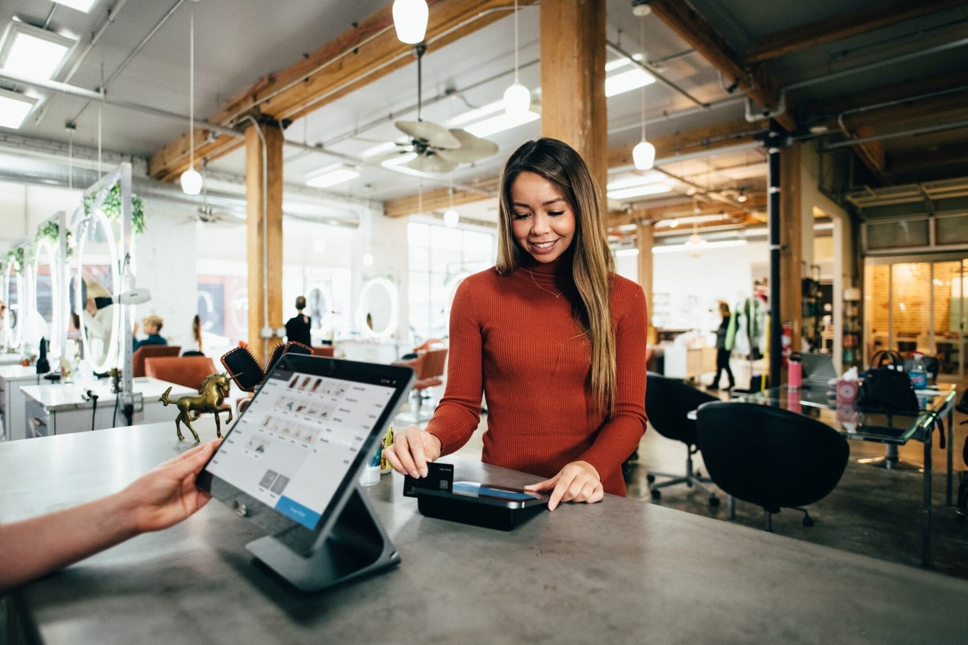 A woman smiles while tapping her credit card on a reader at a modern salon