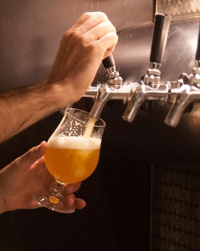 A man pouring a pint of beer in a glass from a tap.