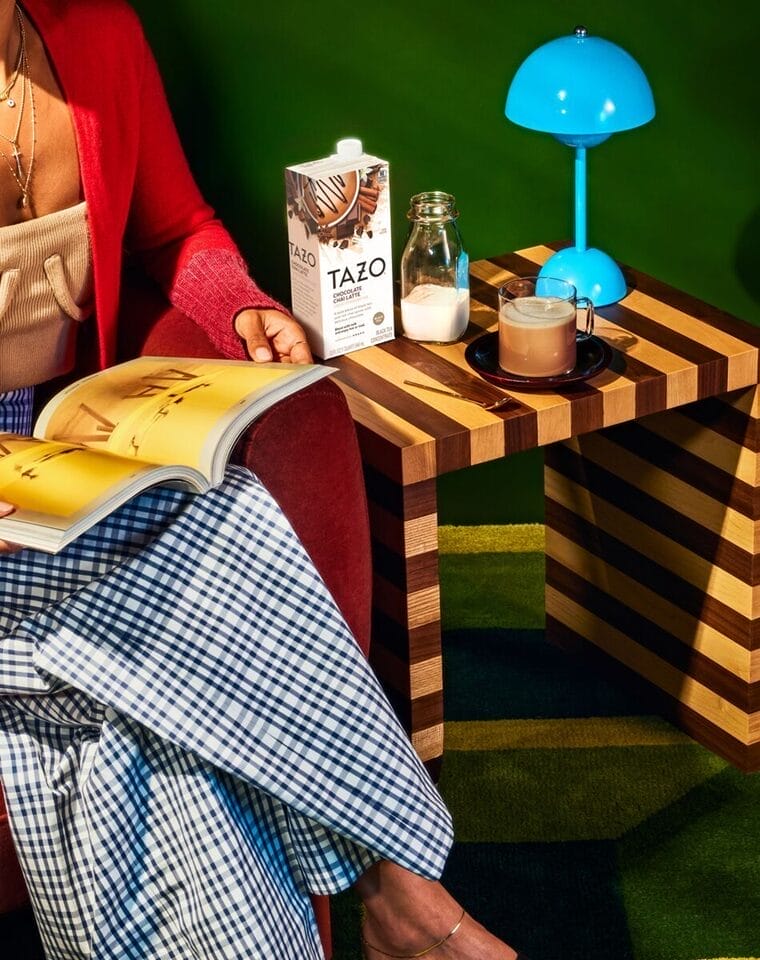 Lady sitting with a box of TAZO chai latte concentrate on the side table.