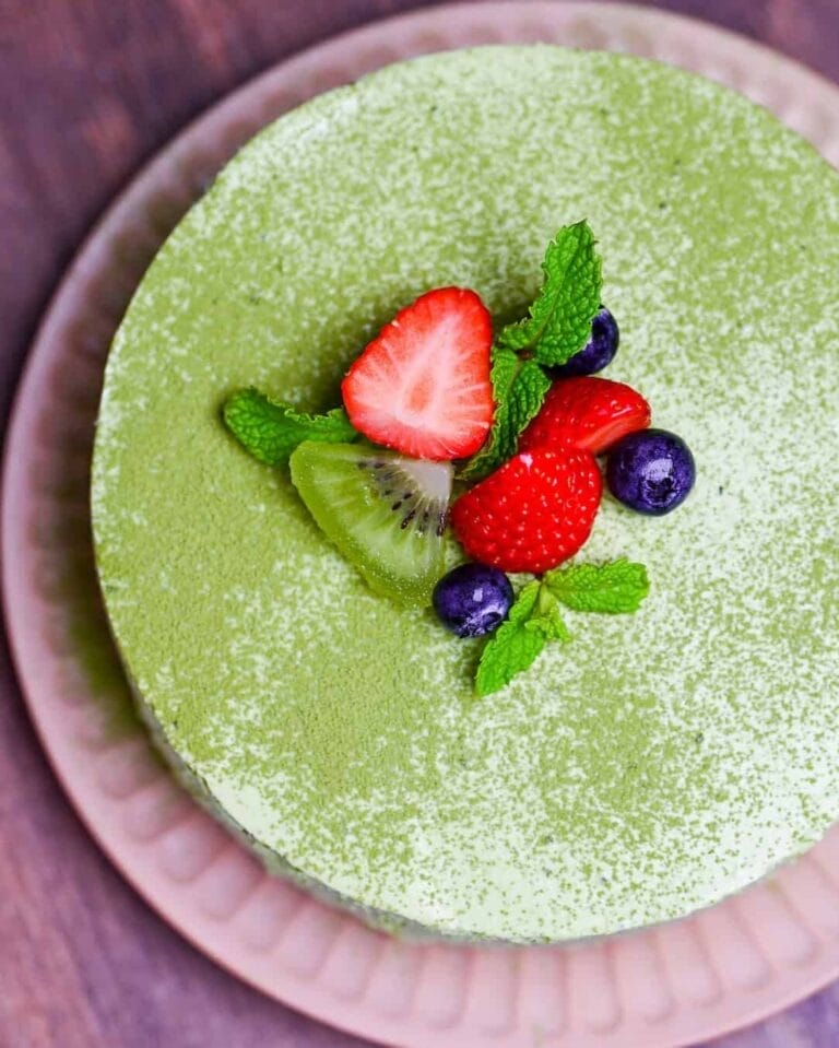 A matcha cheesecake with fruits and dusted matcha powder on top