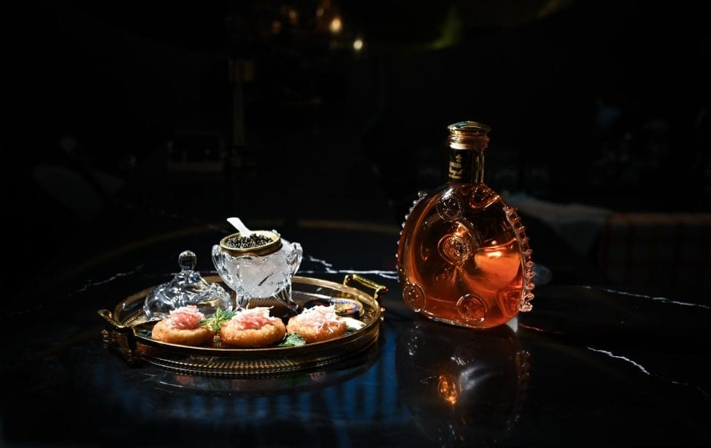 A tray of appetizers with caviar and a bottle of liquor from The one caviar bar