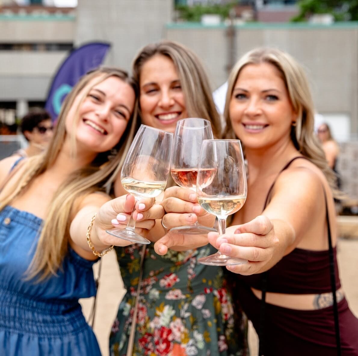 Three women smiling and holding up glasses of white and rosé wine.