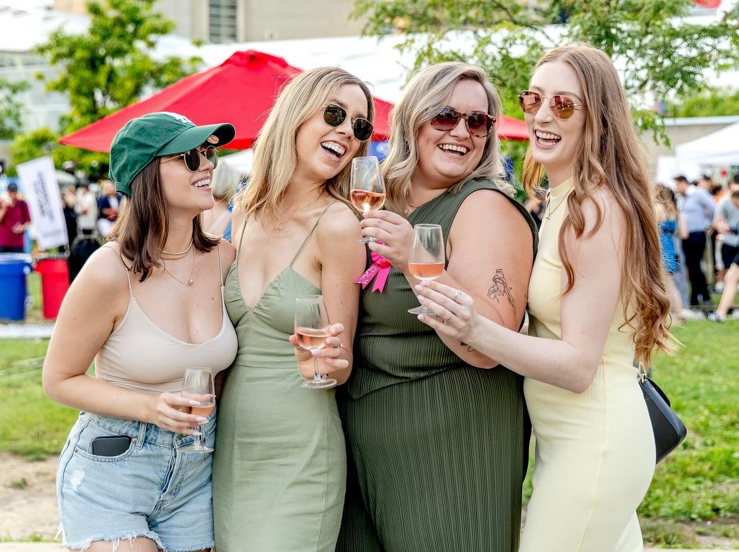 Four women laughing and holding glasses of rosé, having a great time outdoors.