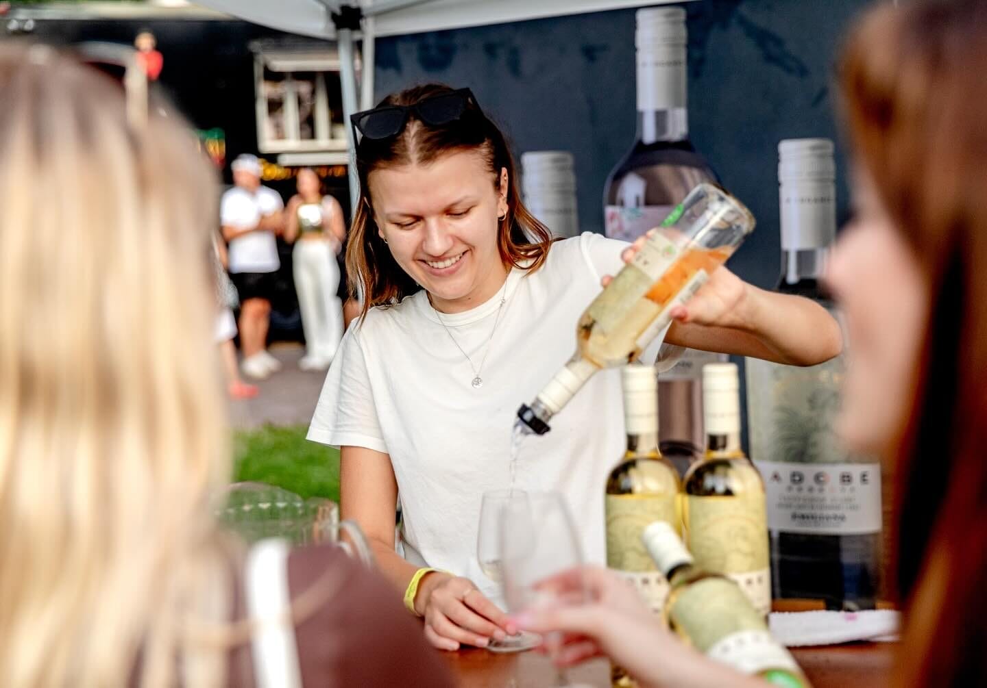 A vendor smiling while pouring a glass for attendees, with bottles displayed on the table.