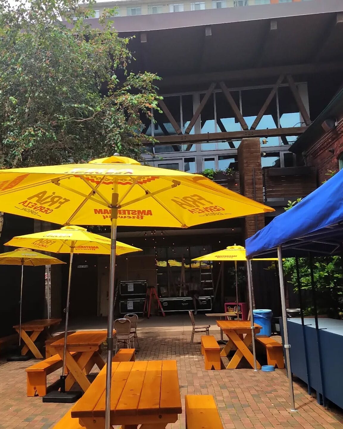 A sunny summer patio in Toronto’s Distillery Historic District featuring yellow Amstel umbrellas, wooden picnic tables, and a cozy atmosphere