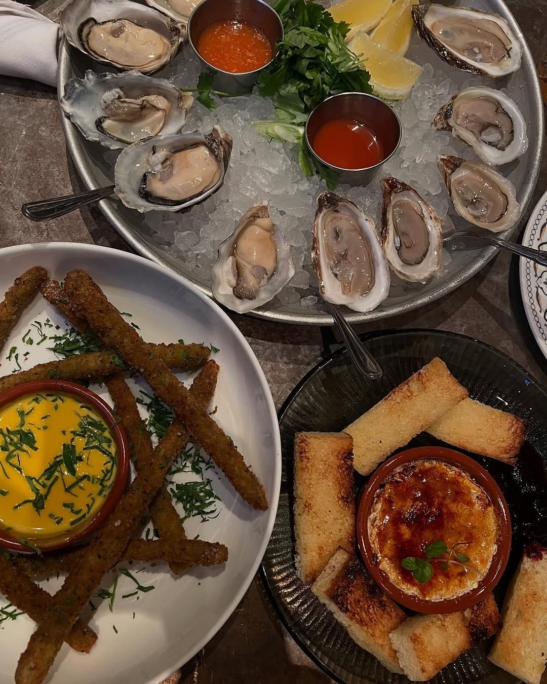A seafood platter with fresh oysters on ice, lemon wedges, cocktail sauce, and herbs at a summer patio in Toronto’s Distillery Historic District