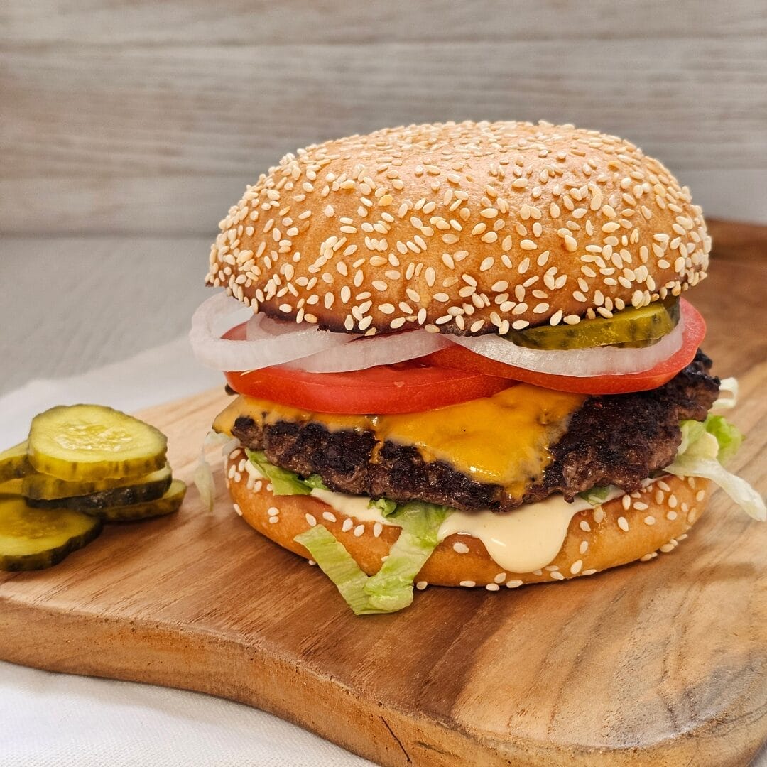 Beef burger with tomato, onion, cheese and lettuce placed on a wooden cutting board.