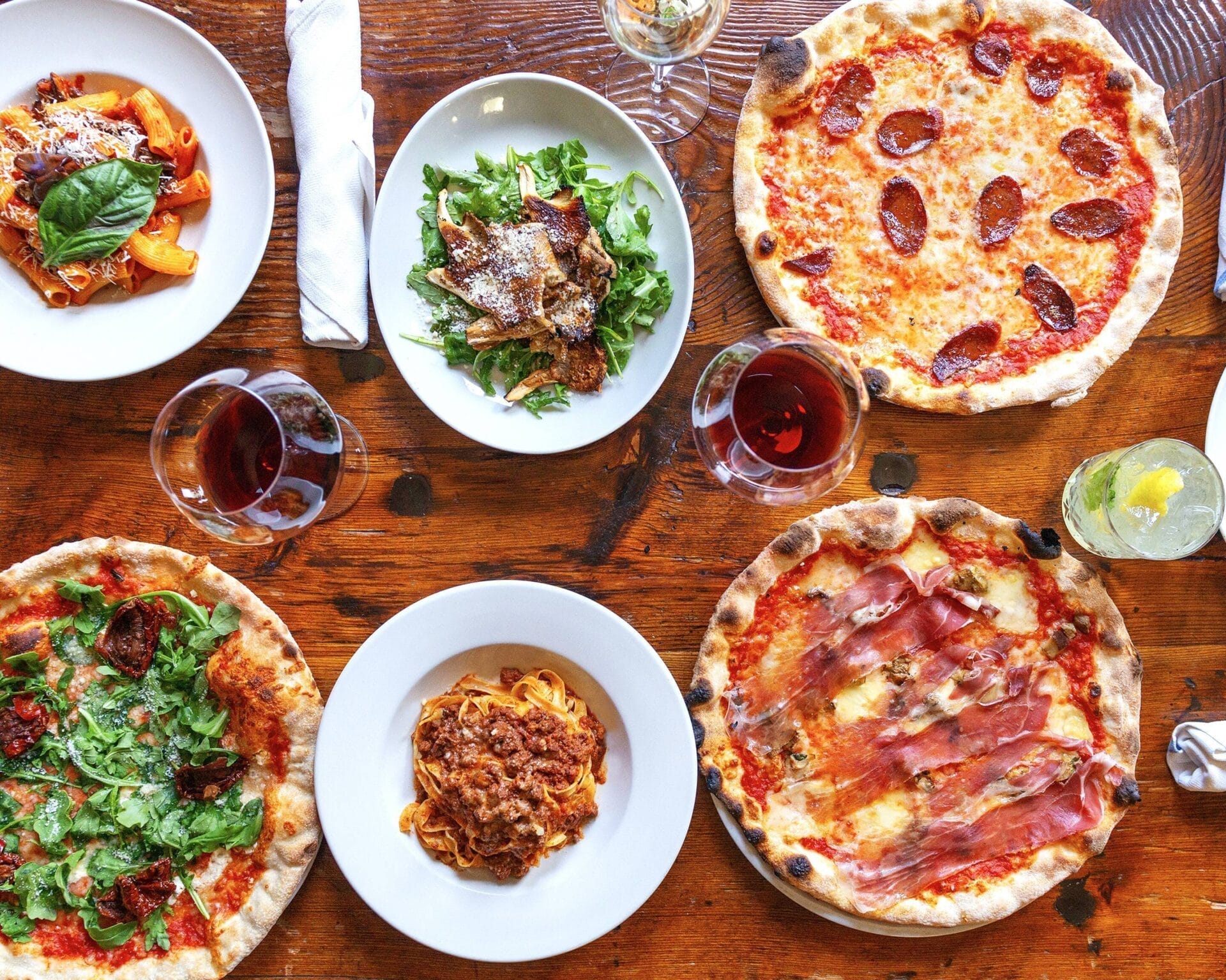 italian dinner on a table, including pasta, salad, pizza, wine