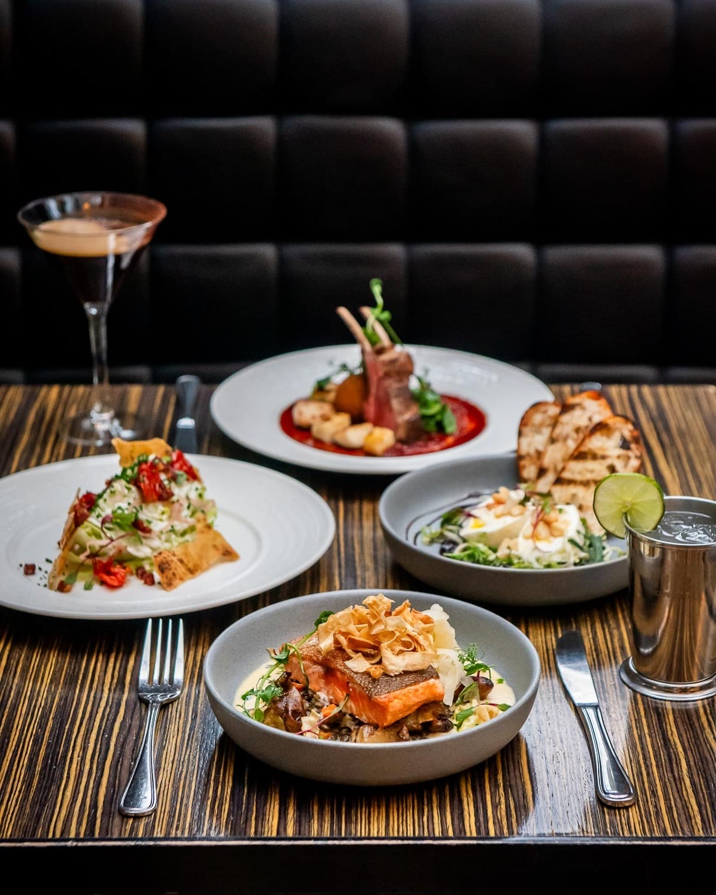 A dining table featuring four plates of various dishes alongside a glass of wine, ready for a meal.