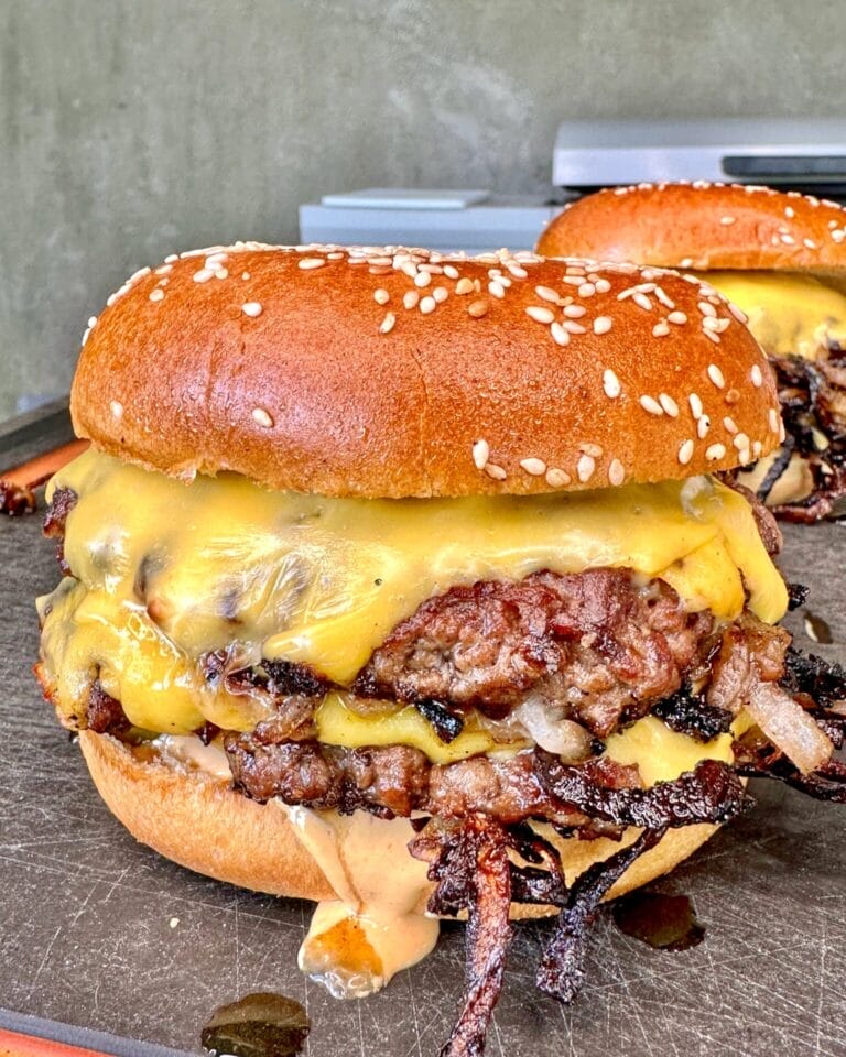 Close-up of a juicy smash burger with caramelized onions, melted cheese, and a toasted sesame seed bun, served on a cutting board. Perfect for Father’s Day lunch or dinner.