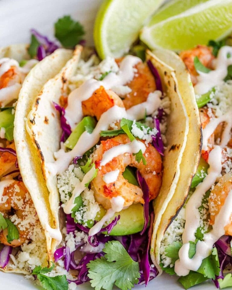 Shrimp Tacos with Spicy Lime Crema, featuring plump shrimp, fresh avocado slices, purple cabbage, cilantro, and cotija cheese, all topped with a drizzle of creamy lime sauce on warm corn tortillas.