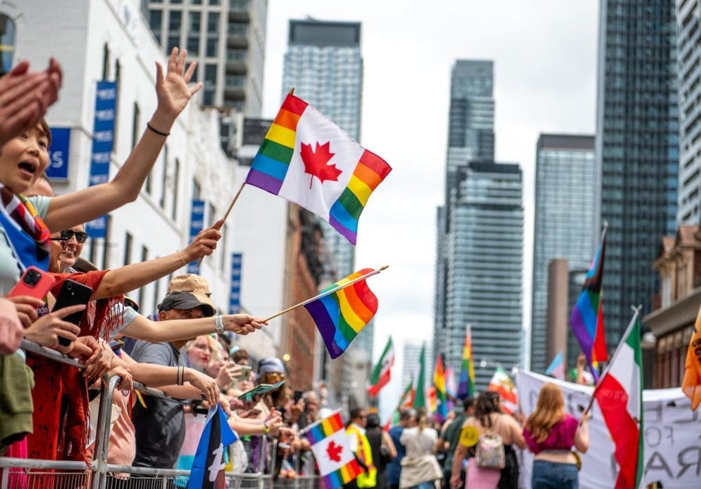 Toronto Summer Festivals You Can’t Miss This June with Pride Toronto parade crowds marching and waving flags in support of LGBTQ+ members.