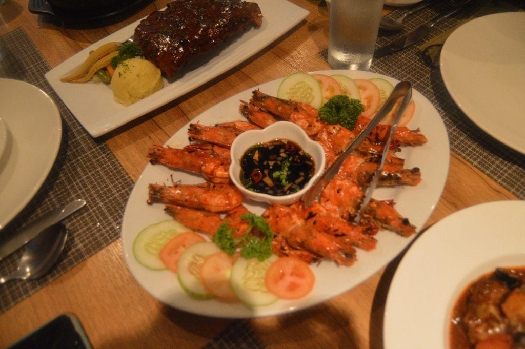 A delicious seafood dining setup featuring a large platter of grilled prawns arranged neatly around a dipping sauce in the center.